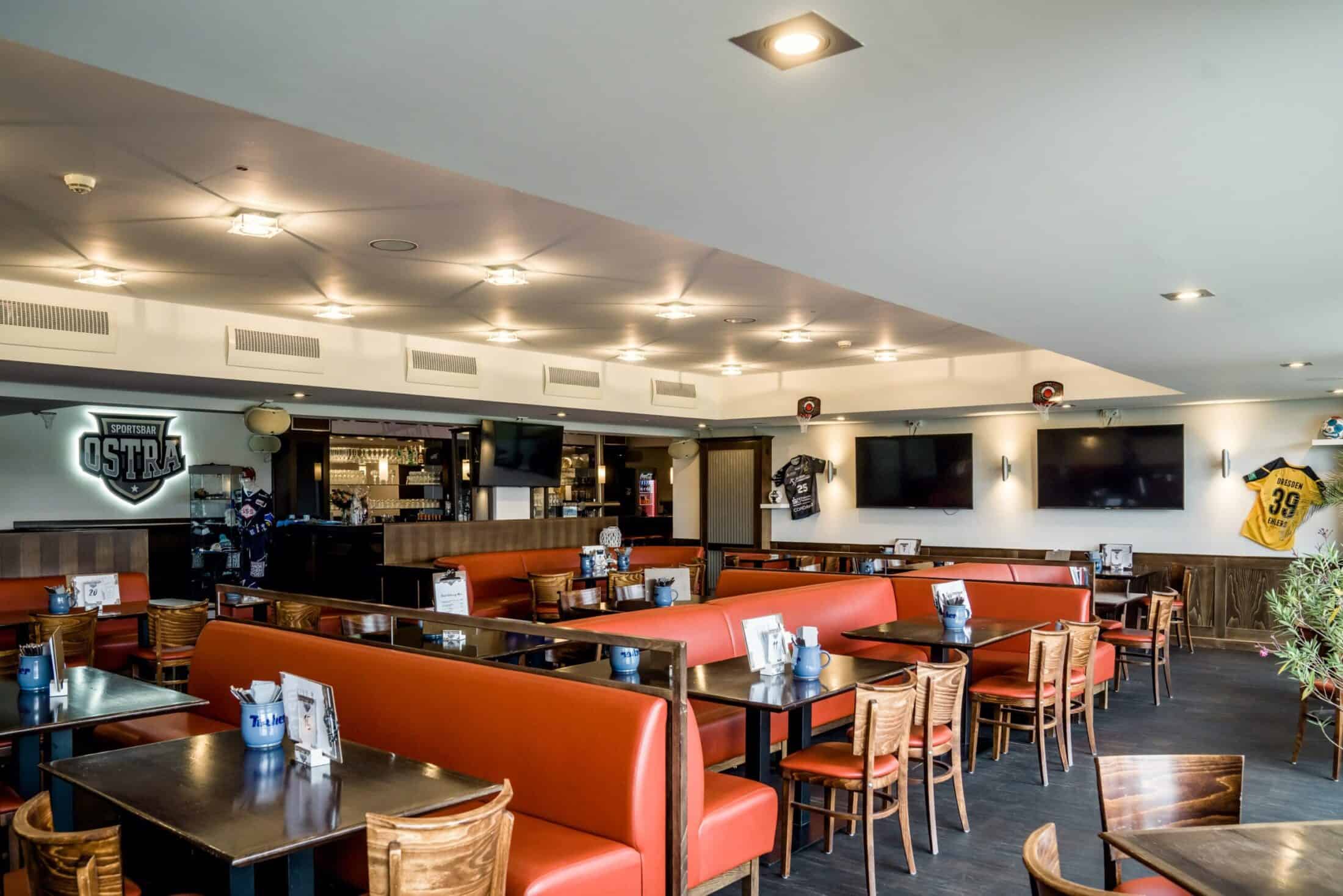 Gastraum der Sportsbar Ostra mit orangefarbenen Bänken und Bildschirmen